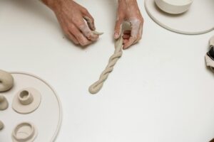 Hands shaping clay to create candle holders, showcasing handmade craft artistry on a clean white surface.